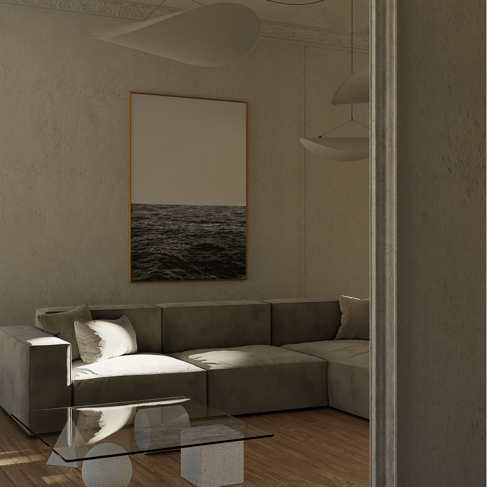 A modern living room scene featuring a gray sectional sofa, a glass coffee table, a wire chair, and a large vertical framed print of an ocean landscape on the wall.