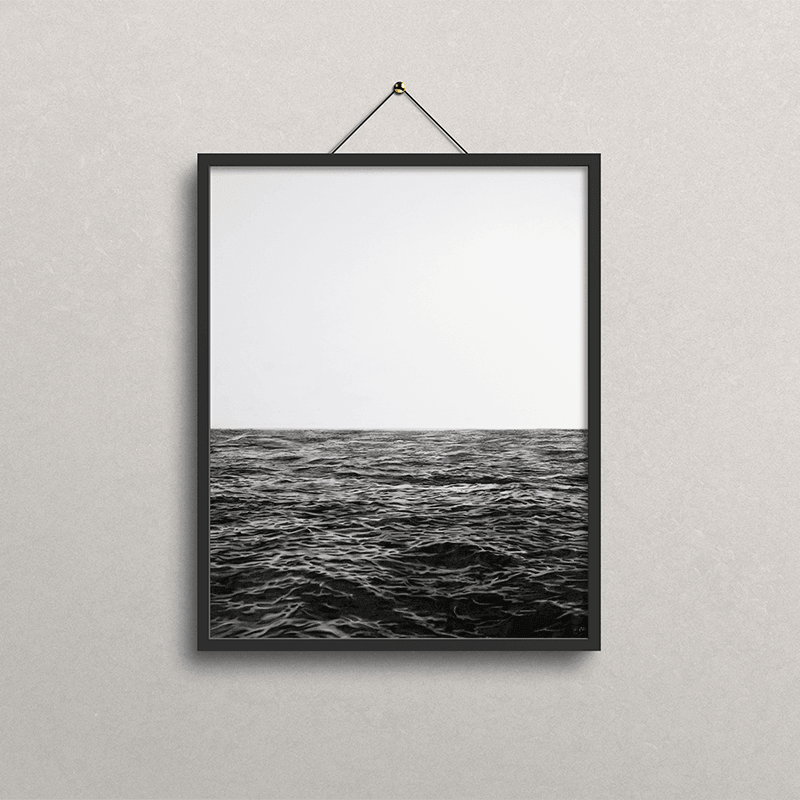 A black-framed wall art print hanging on a light gray textured wall. The print shows a black-and-white seascape photorealistic drawing with a pale sky above dark ocean water.
