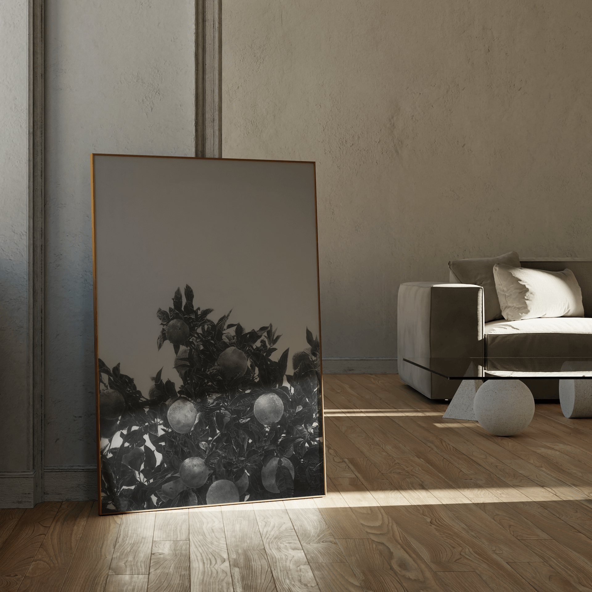 A large vertical framed art print featuring a black and white drawing of an orange tree, leaning against a textured wall in a modern, minimalist living room with a gray sofa and light wood flooring.