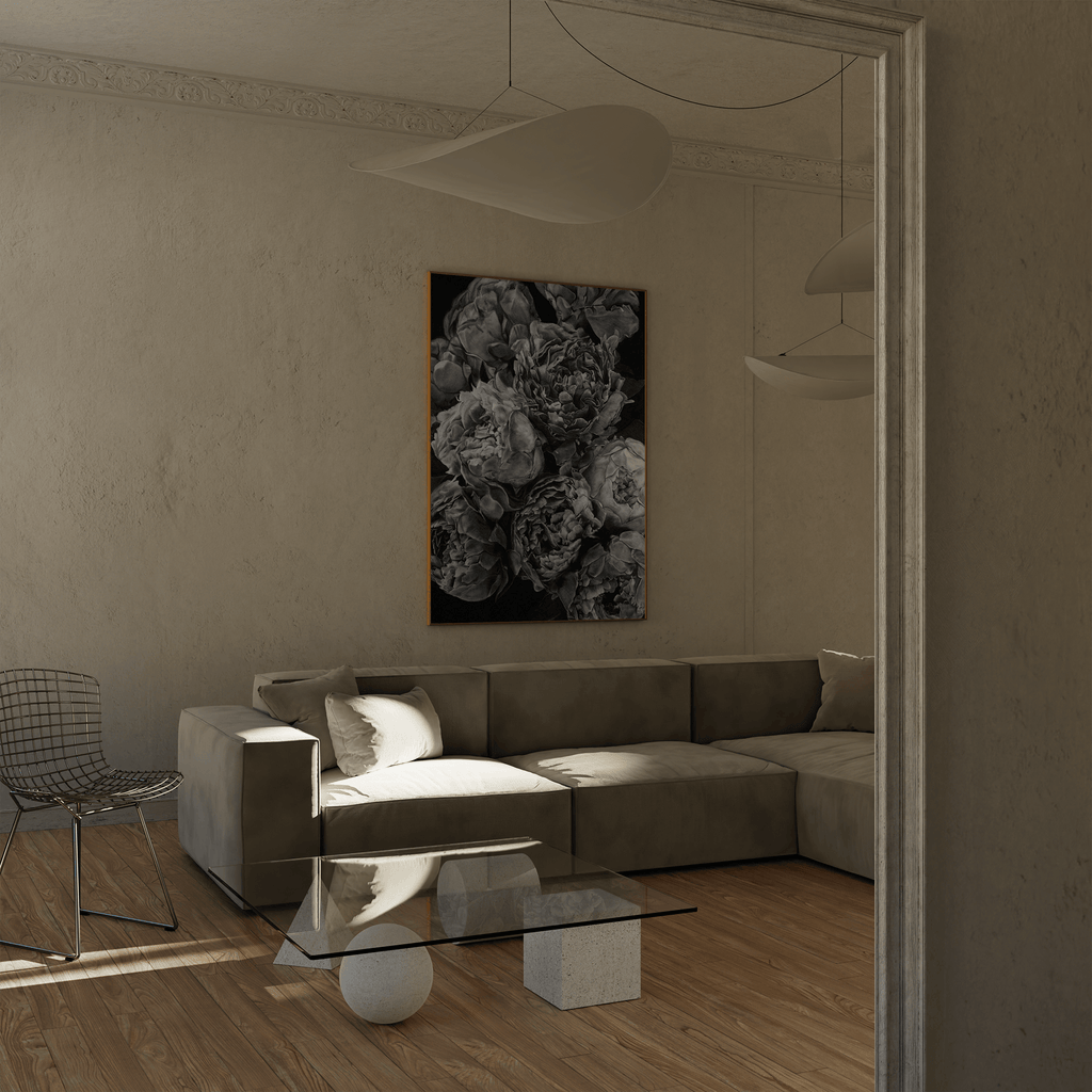 A black and white photorealistic drawing of peonies wall art print, displayed in a modern living room setting above a gray sectional sofa.