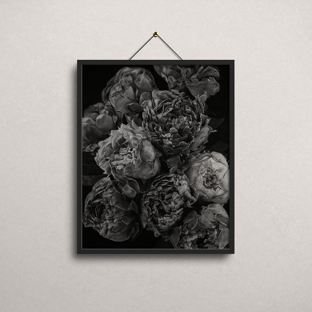 A framed black and white floral art print depicting peonies, hanging from a thin cord against a light textured wall.